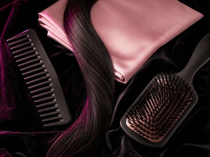 Paddle brush, wide-tooth comb and silk pillowcase next to a hair extension